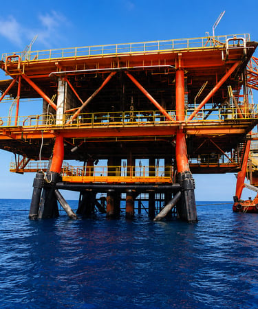 An offshore oil rig platform and drilling equipment standing in the deep blue ocean water.