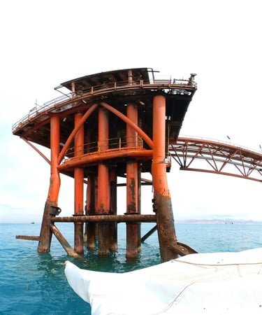 An offshore oil rig platform with weathered orange pillars standing in blue ocean water.