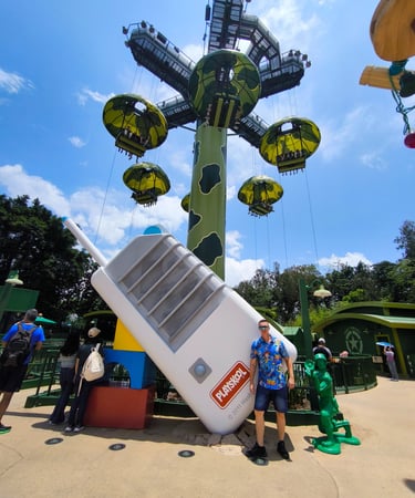 Hombre posando en la zona de Toy Story Land de Hong Kong Disneyland, con la atracción Toy Soldier Pa