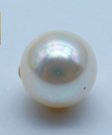 Macro shot of a pearl's surface under a soft light, showing a clean and smooth texture with almost no visible imperfections. Background in Soft Pearl Blue.