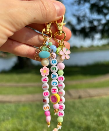 Mano sosteniendo dos llaveros, hecho de cuentas con letras y flores