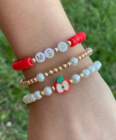 Pulseras colocadas en el brazo, con perlas, letras y un charm con figura de manzana
