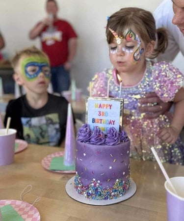 Young girl leaning over a birthday cake, unicorn painted on her face