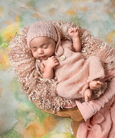 a baby girl sleeping in a basket with a pink blanket