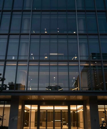 Low-key cinematic lighting on a modern architectural glass facade of a premium medical center at dusk, deep navy shadows, subtle brushed gold highlights, off-center composition.