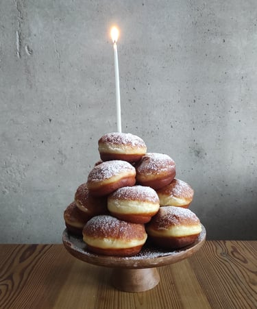 Pączki ułożone w stos na paterze z wbitą urodzinową świeczką na czubku