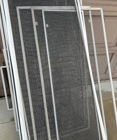 A stack of aluminum window screens with black mesh leaning against a garage door for replacement.