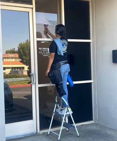 Professional window cleaner using a squeegee on a commercial glass door while standing on a ladder.