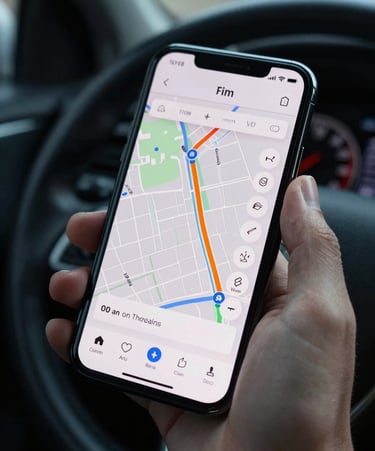 Close-up of a hand holding a phone showing a map routing interface with minimal UI, soft north-facing ambient light, dark car interior visible in background, precise framing