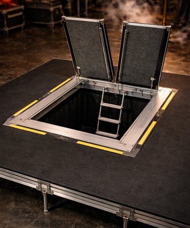 Open stage trapdoor with ladder access on a professional theater platform with safety markings.