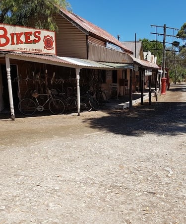 A vintage bike shop and other historic buildings line a dusty street, evoking an old Australian townscape.