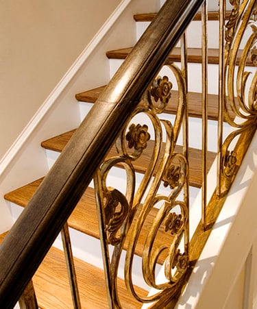 Elegant oak wood staircase featuring an ornamental gold wrought iron railing with floral scrollwork.