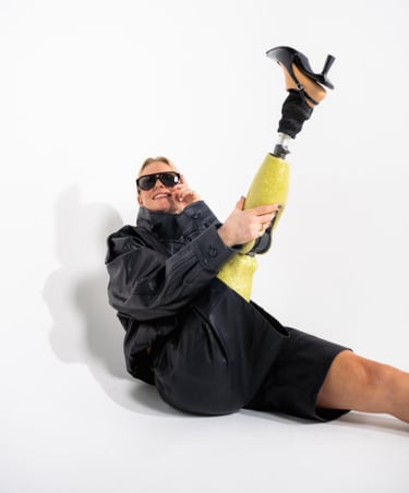 A stylish woman in a black leather jacket wearing a sparkly yellow prosthetic leg and high-heel shoe.