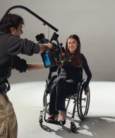 A smiling woman in a wheelchair being filmed by a cameraman with a professional cinema rig in a studio.