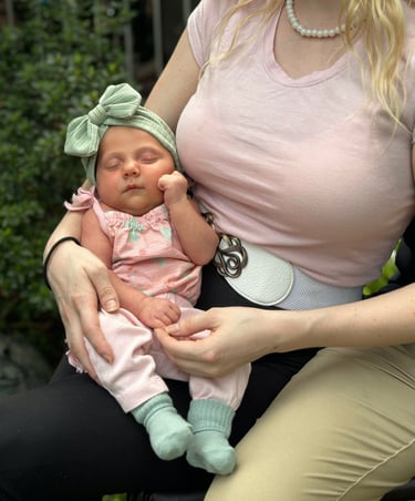A mother in a pink shirt holding her sleeping baby in a green bow resting with hand on cheek.