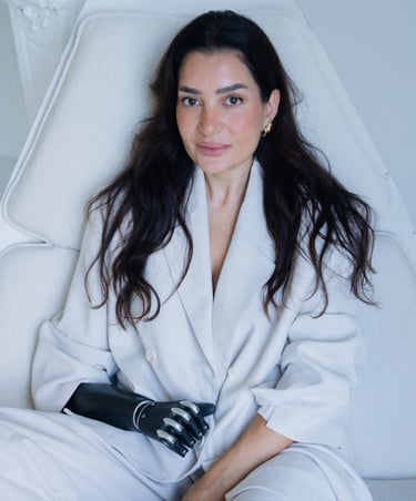 A woman in a white blazer sitting on a white chair with a bionic prosthetic arm.