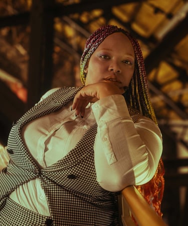 A picture of Lamia, a Black person wearing a gingham vest and white button up shirt
