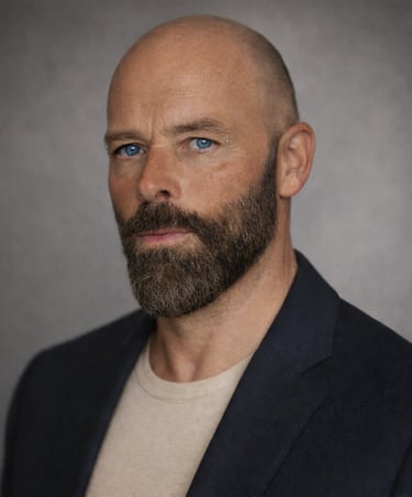 Professional portrait of Damon with blue eyes and a groomed beard wearing a dark blazer.