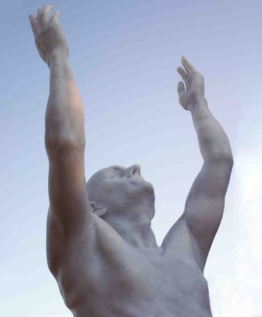 White marble statue of a man reaching his arms up toward a clear blue sky.