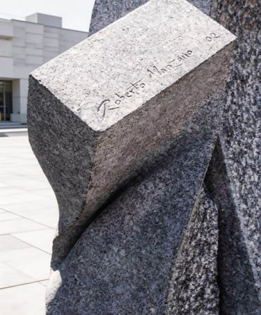 Granite stone sculpture with the signature of artist Roberto Manzano carved into the surface.