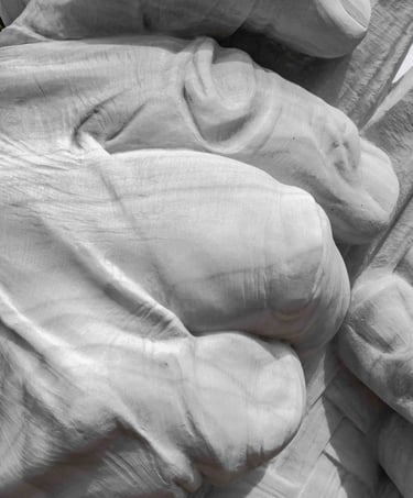 White marble sculpture of large hands weaving a mat with esparto grass on a stone pedestal in a squa