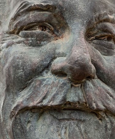 Bronze relief bust of a bearded man mounted on a natural stone rock in an outdoor park setting.