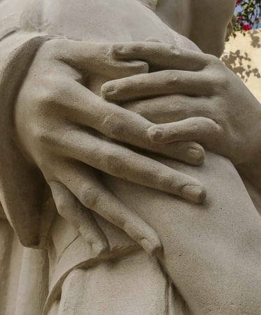 Close-up of stone sculpture showing detailed hands embracing a figure with realistic texture.