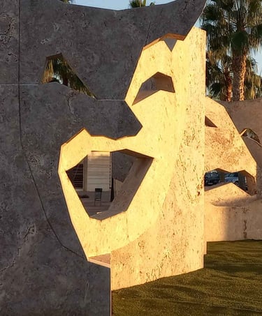 Large stone theater mask sculptures with palm trees in the golden hour sunlight.
