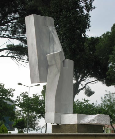 Contemporary abstract marble sculpture with geometric shapes in a public park setting.