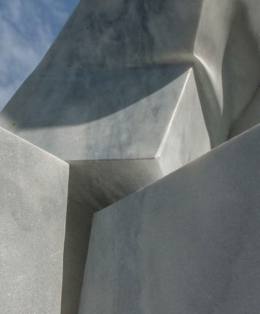 Abstract white marble sculpture with geometric stone shapes and sharp shadows against a blue sky.