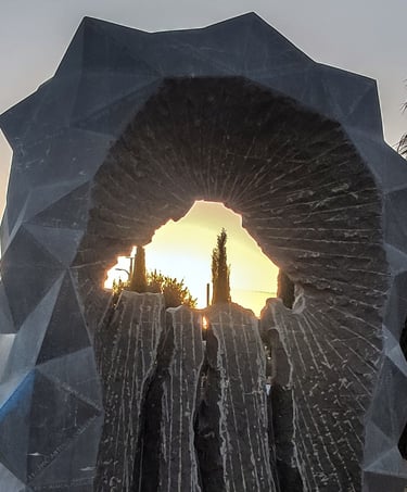 A geometric stone monument framing a golden sunset landscape through a jagged central cutout.