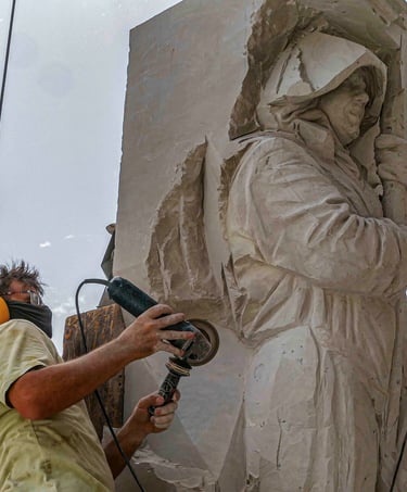 Professional sculptor using a power grinder to carve a detailed stone statue of a hooded figure.