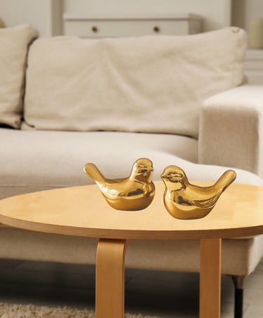 Par de passarinhos decorativos dourados em cerâmica sobre mesa de madeira em sala aconchegante.