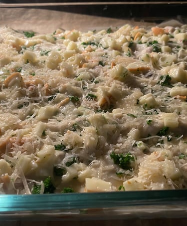 Close-up of uncooked creamy chicken casserole in a glass baking dish, topped with shredded cheese, diced chicken, and herbs