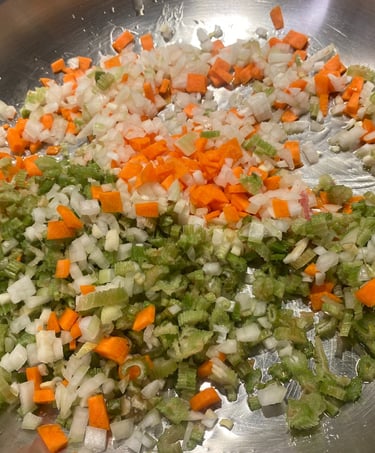 Finely diced carrots, celery, and onions sautéing in a stainless steel pan as a mirepoix base.