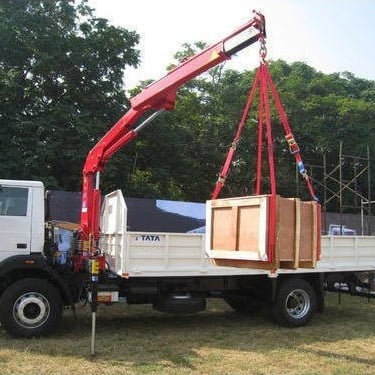 A mini truck-mounted crane lifts a large wooden box onto a truck.