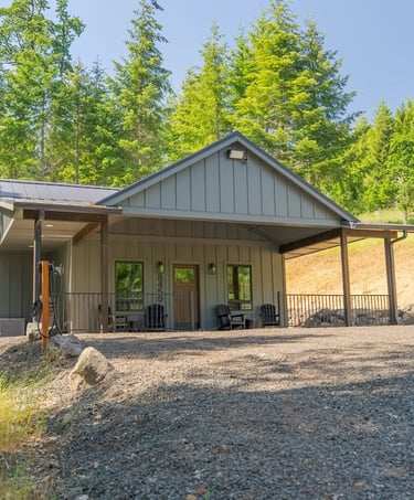 A modern gray board and batten cabin with a metal roof nestled in a lush green forest clearing.