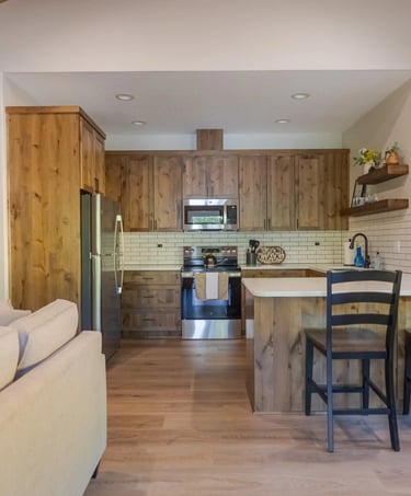 Modern rustic kitchen with wood cabinets, stainless steel appliances, and a breakfast bar with black stools.