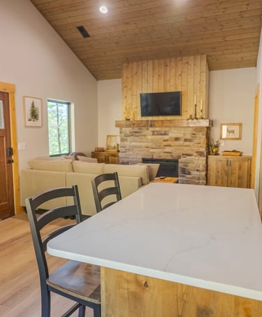 Rustic modern cabin interior with stone fireplace, wood vaulted ceiling, and white kitchen island.