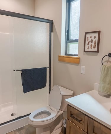 Modern bathroom interior featuring a walk-in shower with sliding glass doors, white vanity, and rustic wall decor.