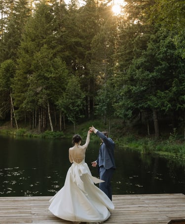 A bride and groom dancing on a wooden dock by a serene lake during an outdoor forest wedding.