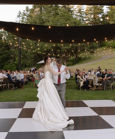 Bride and father dancing on a checkered dance floor at an outdoor wedding reception with string lights.