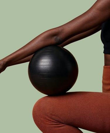 Dark brow arms balance a black weighted medicine ball on their knee for core and stability training.