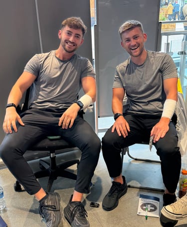 2 first aid trainers demonstrating practical bandage skills while seated with training equipment 
