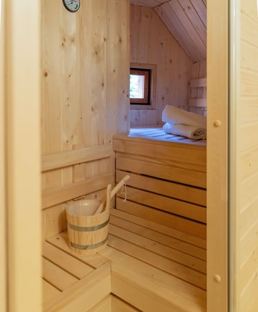 Interior of a modern wooden home sauna with tiered cedar benches, a water bucket, and white towels.