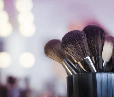 Makeup brushes in a black cup over a blurred, well-lit studio background