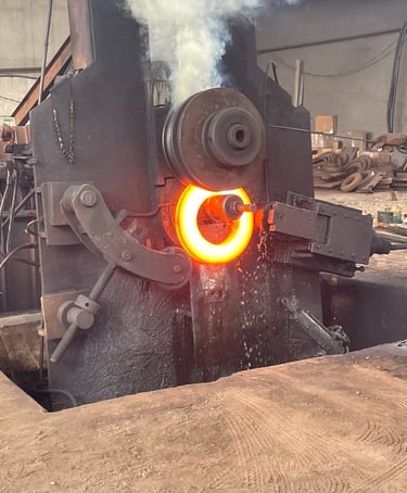 Industrial ring rolling machine shaping a glowing red-hot metal ring in a steel forging factory.