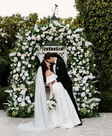 a bride and groom kissing in front of a floral arch