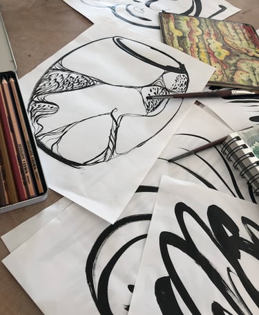 A display of black ink drawings with a vase sketch on top, pencils and notebook