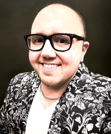 Smiling bald man wearing black thick-rimmed glasses and a floral print blazer.